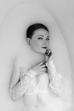 Žena ve vaně – černobílá fotografie, žena v bílém krajkovém prádle ve vaně z části ponořená do neprůhledné tekutiny