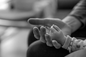 Dlaně – černobílá fotografie, dlaně ženy, v ní měkce spočívá drobná ručka novorozence